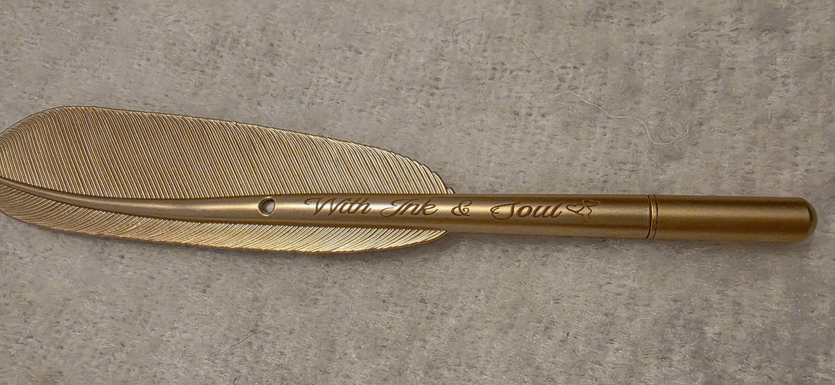 A gold-colored metal feather quill pen with engraved text reading 'WILLIAM H. DAVIS', resting on a textured gray background.